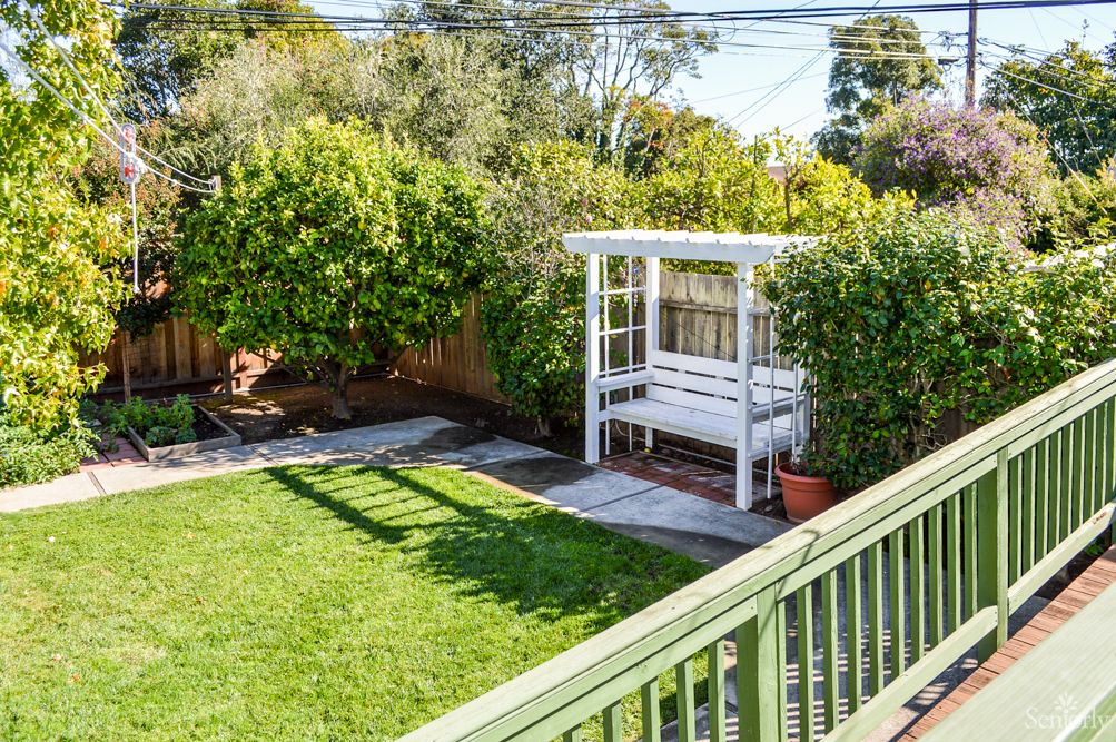 A cozy backyard with a lush green lawn and a white pergola seating area surrounded by tall hedges.