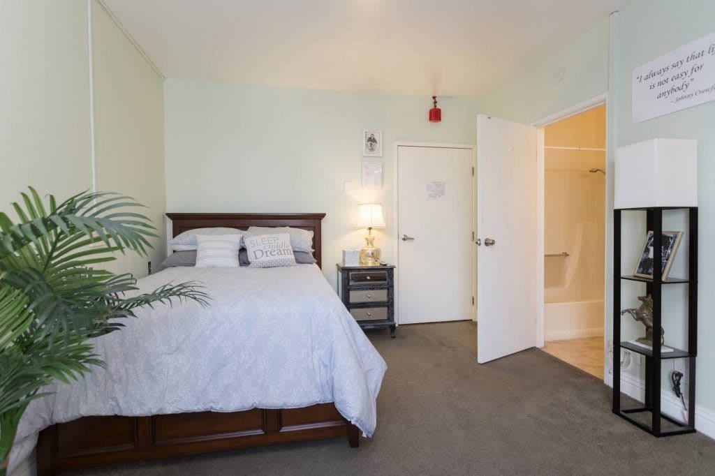 A cozy bedroom with a wooden bed, nightstand, and open door leading to a bathroom.