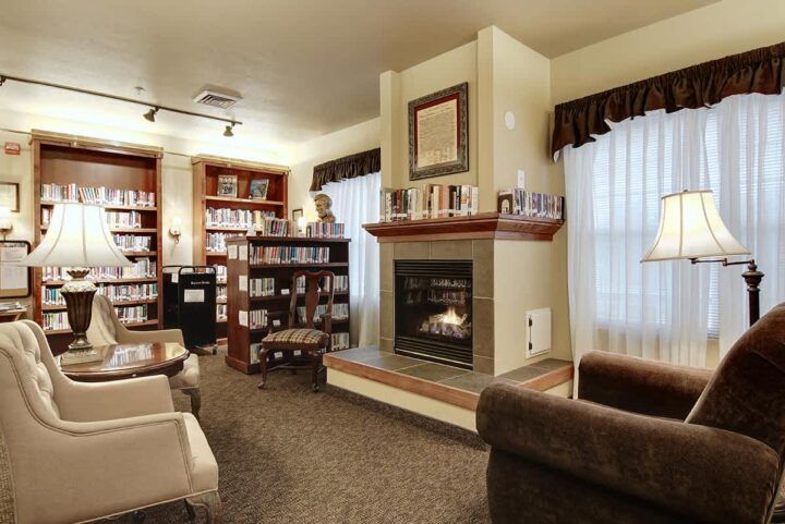 A cozy library with bookshelves, a fireplace, and comfortable seating for reading.