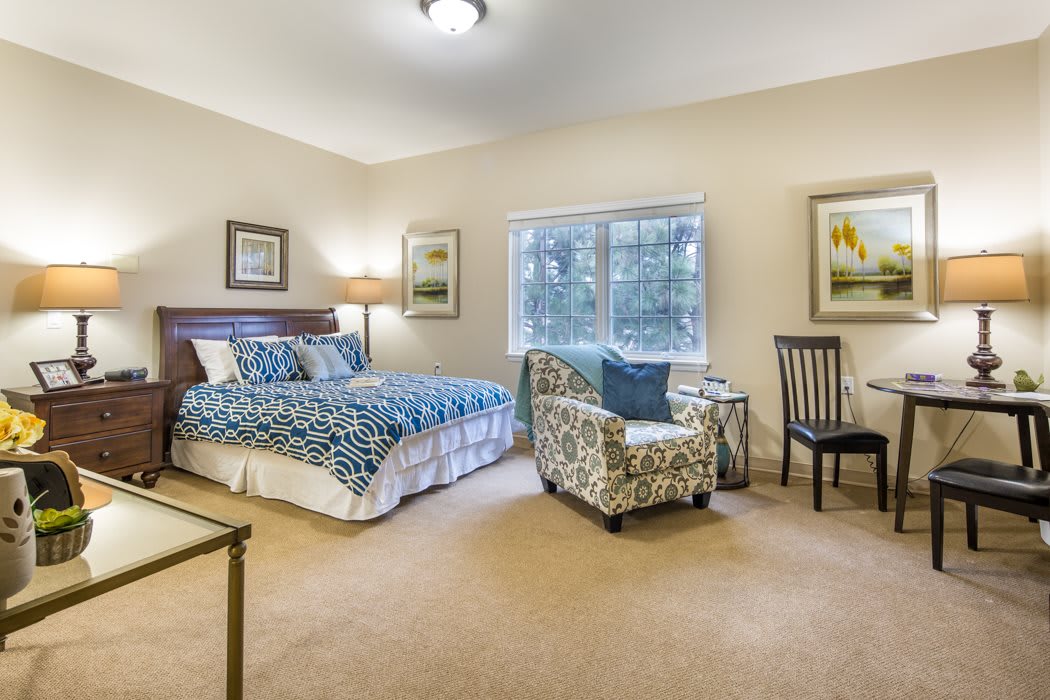 A cozy bedroom with a blue-patterned bedspread, two chairs, and a large window.