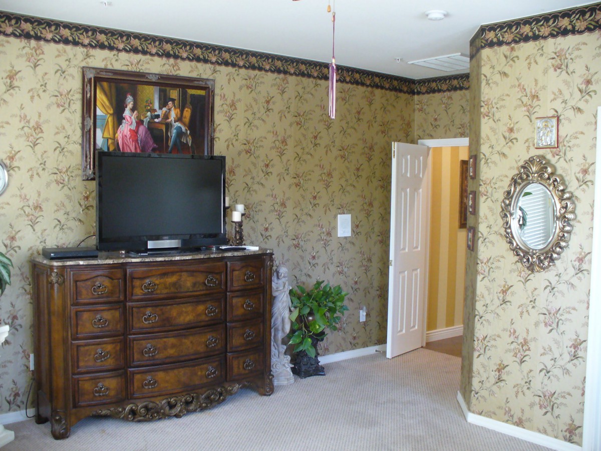 A bedroom featuring antique furniture and a television, with ornate wallpaper and a decorative mirror.