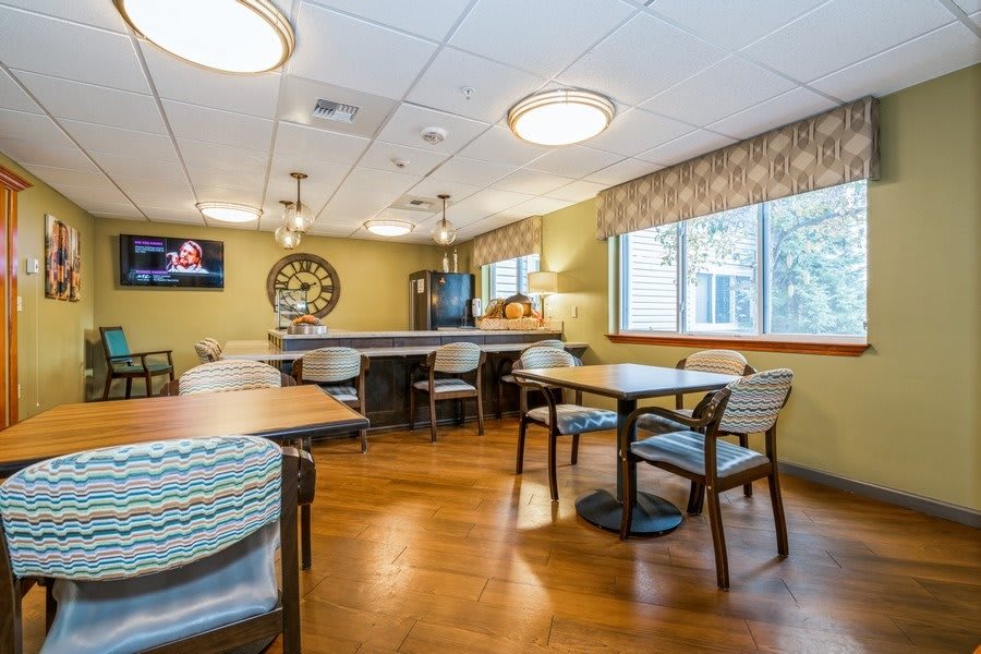 A cozy dining area with wooden flooring, tables, chairs, and a television on the wall.