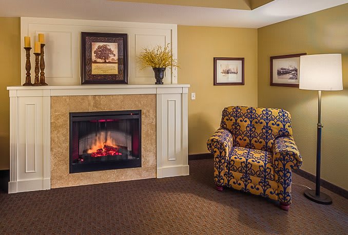 A cozy living room features a fireplace, patterned armchair, and decorative artwork.