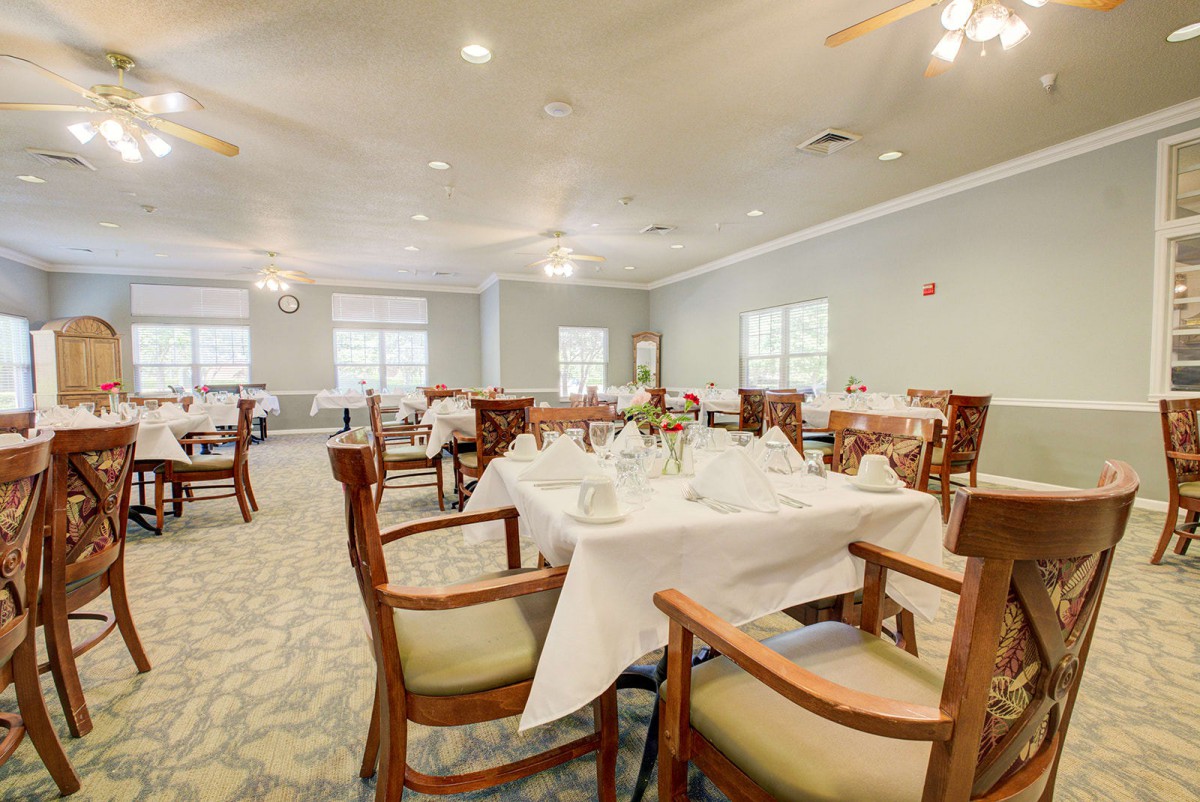 An elegant dining room with neatly set tables and chairs, featuring white tablecloths and warm lighting.