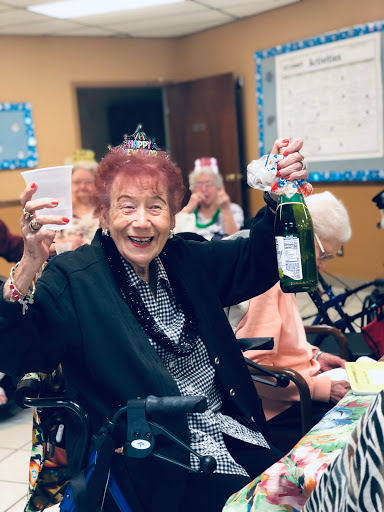 A joyful moment captured during a celebration at a community center, where an elderly woman happily raises her glass and bottle.