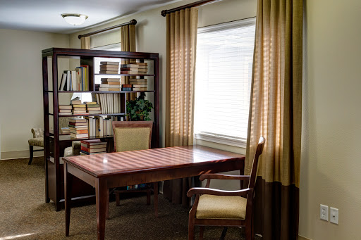 A cozy and organized home office featuring a wooden desk, comfortable chair, and a bookshelf filled with books.