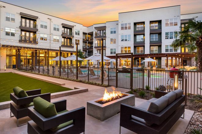 Modern apartment complex featuring an inviting outdoor space with a pool and fire pit at sunset.