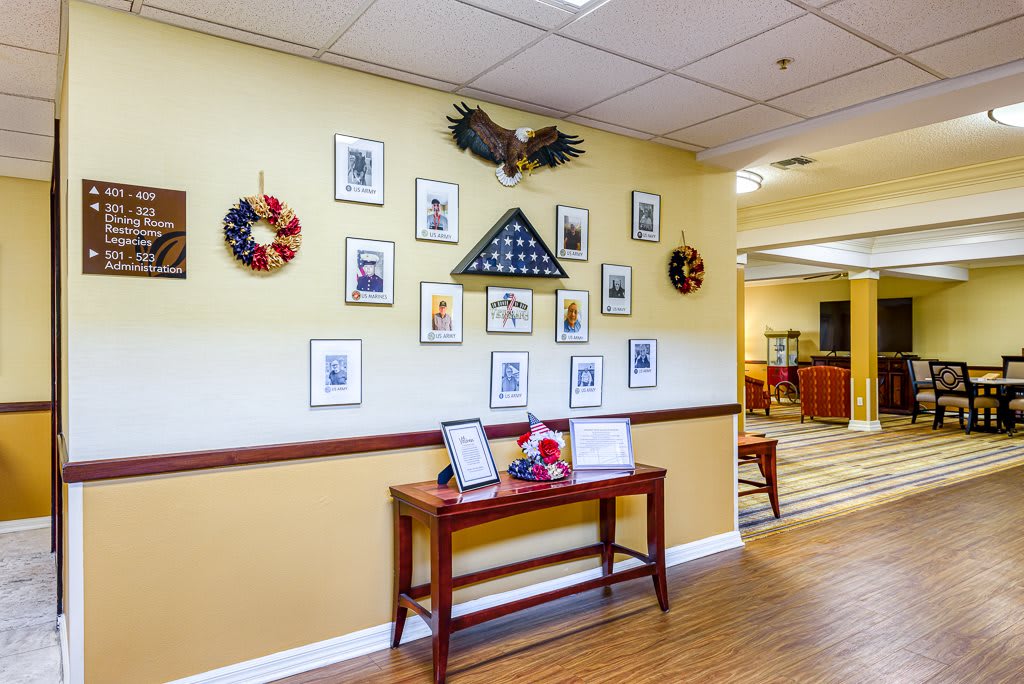 A hallway featuring a gallery wall with framed photographs, a memorial flag display, and patriotic decorations above a wooden table holding various items.