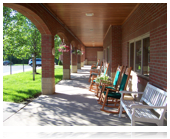 A shaded porch with several rocking chairs and outdoor seating.
