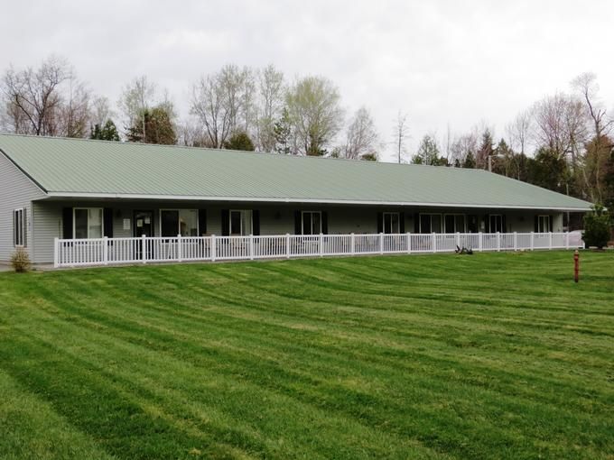 A long building with a green roof and white fence, surrounded by a well-maintained lawn and trees in the background.