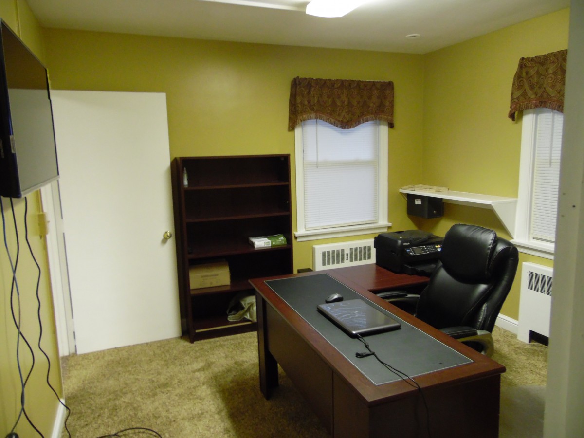 An office room with a large desk, leather chair, and bookshelf.