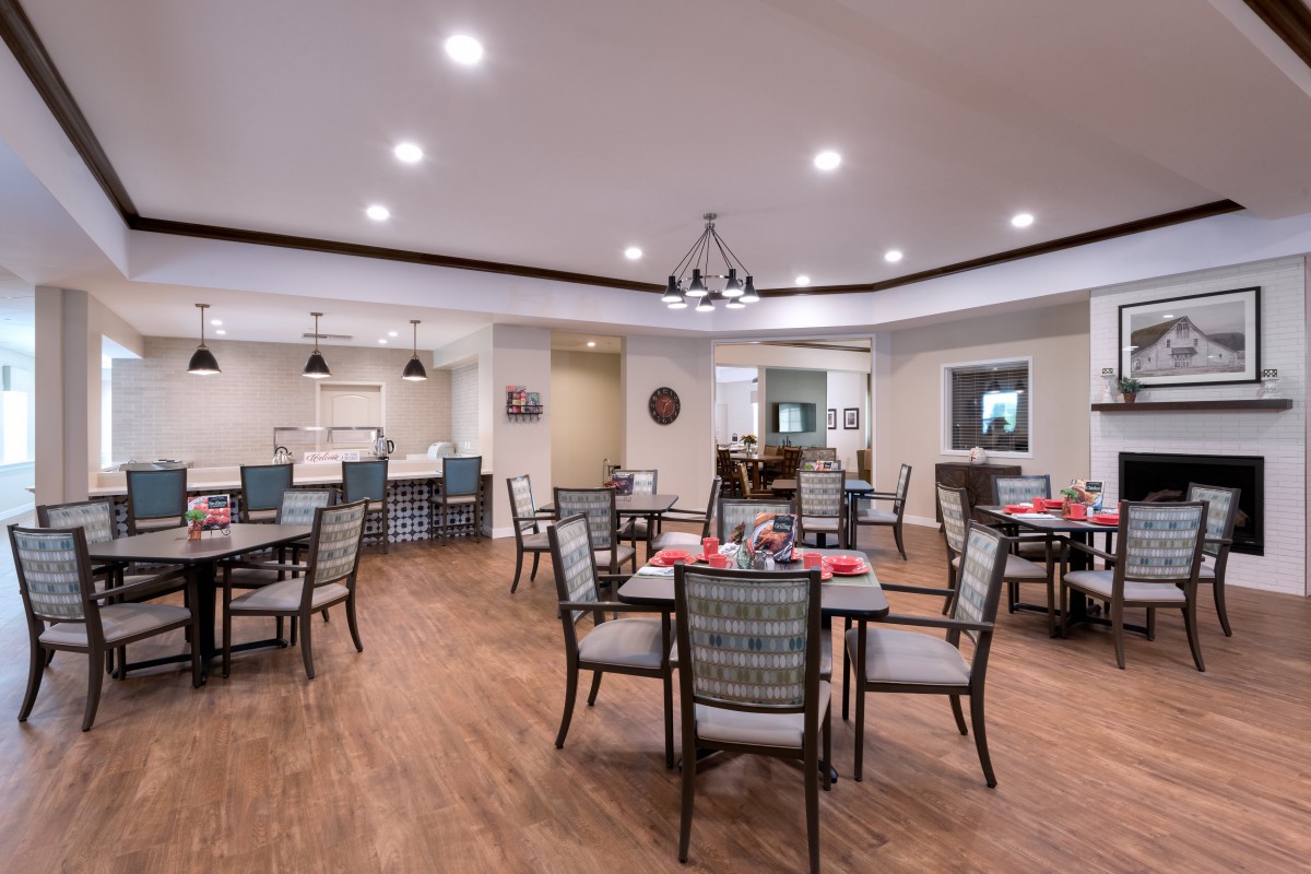 A modern dining area with neatly arranged tables and chairs, featuring elegant lighting and a wooden floor.