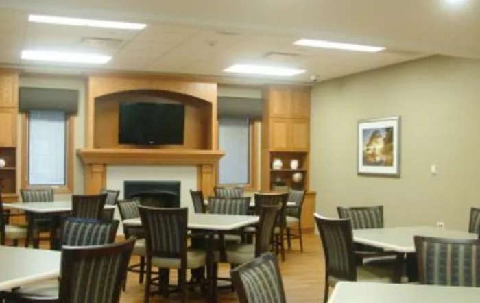 A modern dining room with multiple tables and chairs, featuring a fireplace and a wall-mounted television.