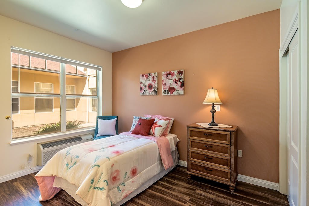 Cozy bedroom with a single bed, side table, lamp, and floral decor.