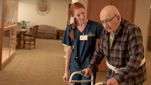 A nurse assists an elderly patient with a walker, providing support and care in a rehabilitation setting.