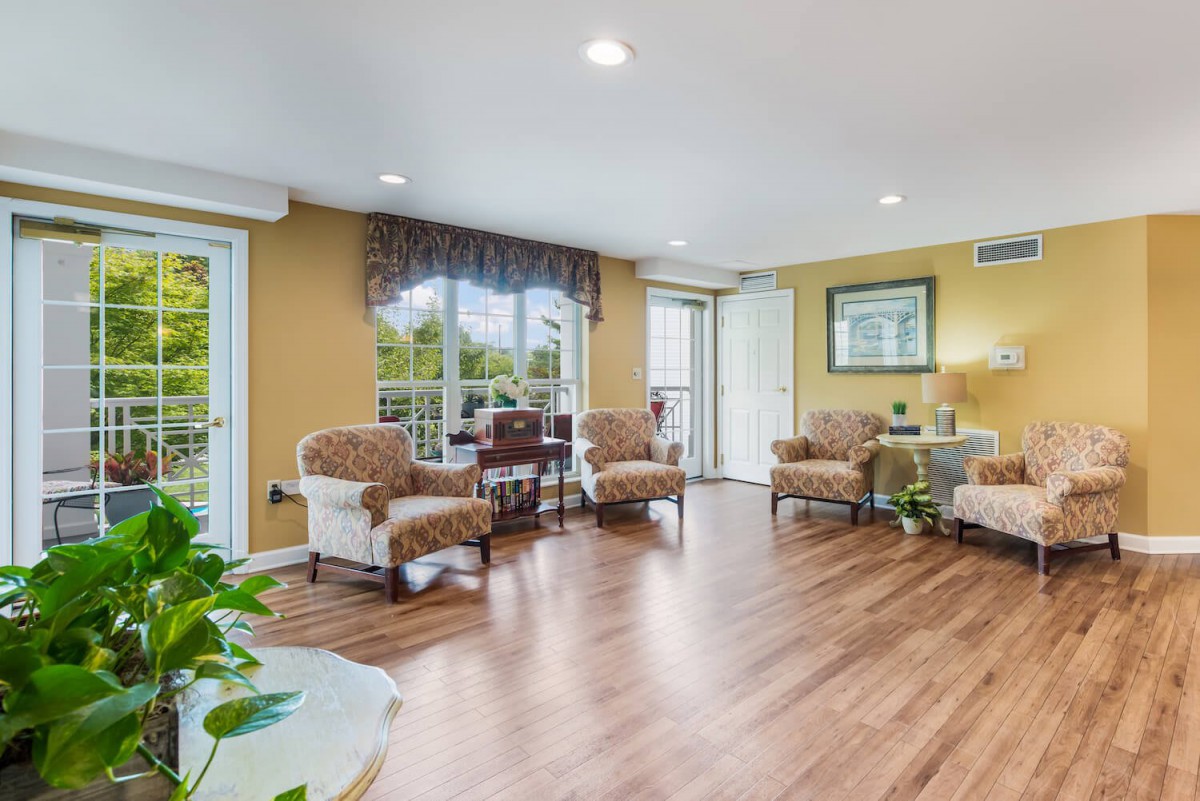 A bright living room featuring elegant furniture and natural wood flooring, illuminated by abundant natural light from large windows.