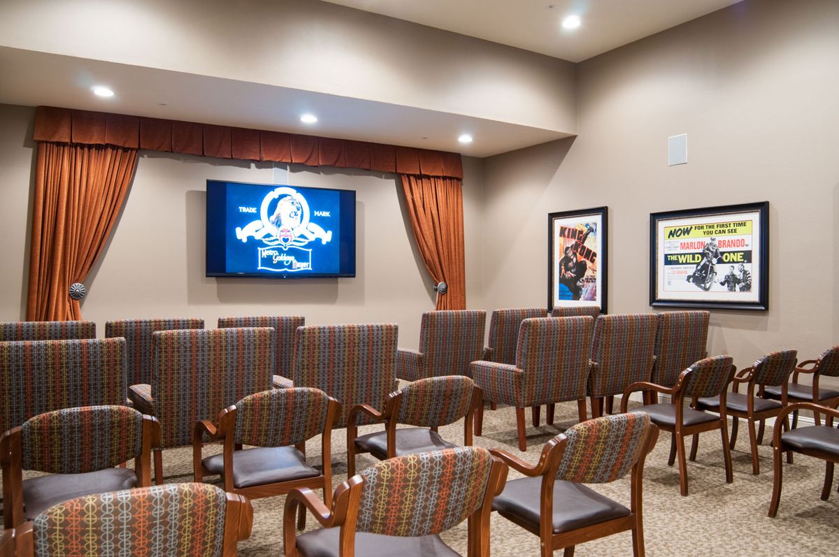 A small conference or waiting area with rows of cushioned chairs facing a mounted television.