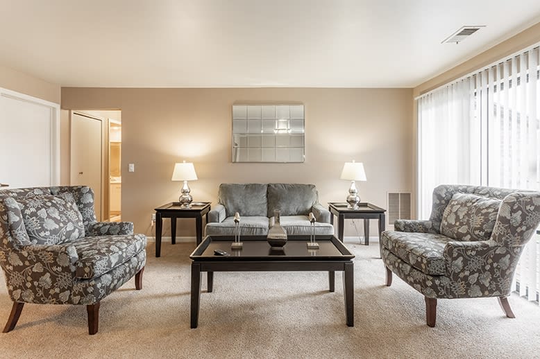 A cozy living room with a sofa, armchairs, and coffee table, warmly lit by lamps on side tables.