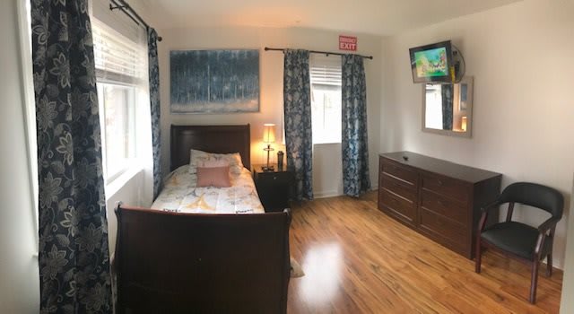 A cozy bedroom with a single bed, wooden flooring, and a wall-mounted TV.