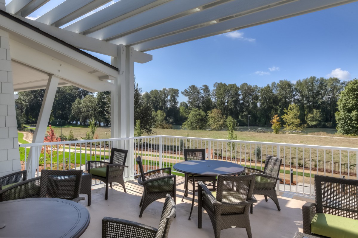 Outdoor patio area with tables and chairs under a pergola, surrounded by nature.