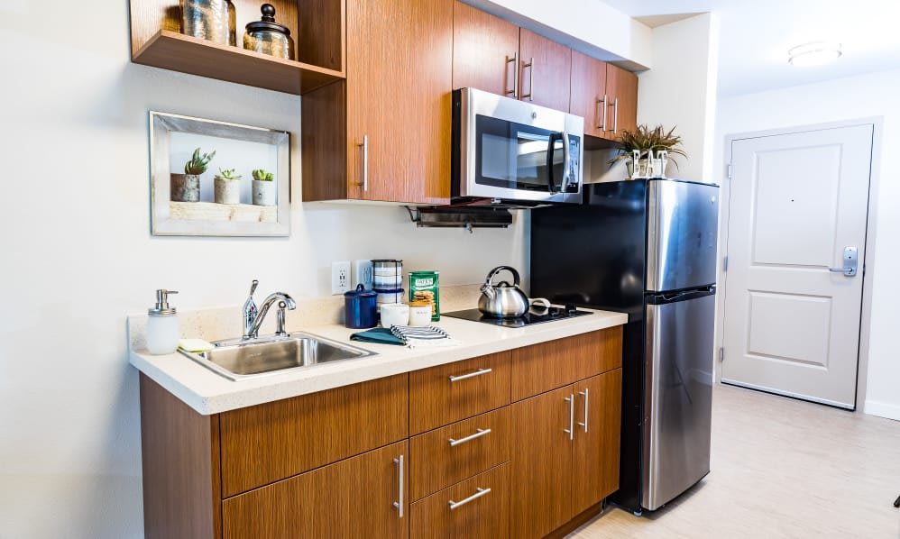 A modern kitchen with wooden cabinetry, featuring a microwave, refrigerator, and sink.
