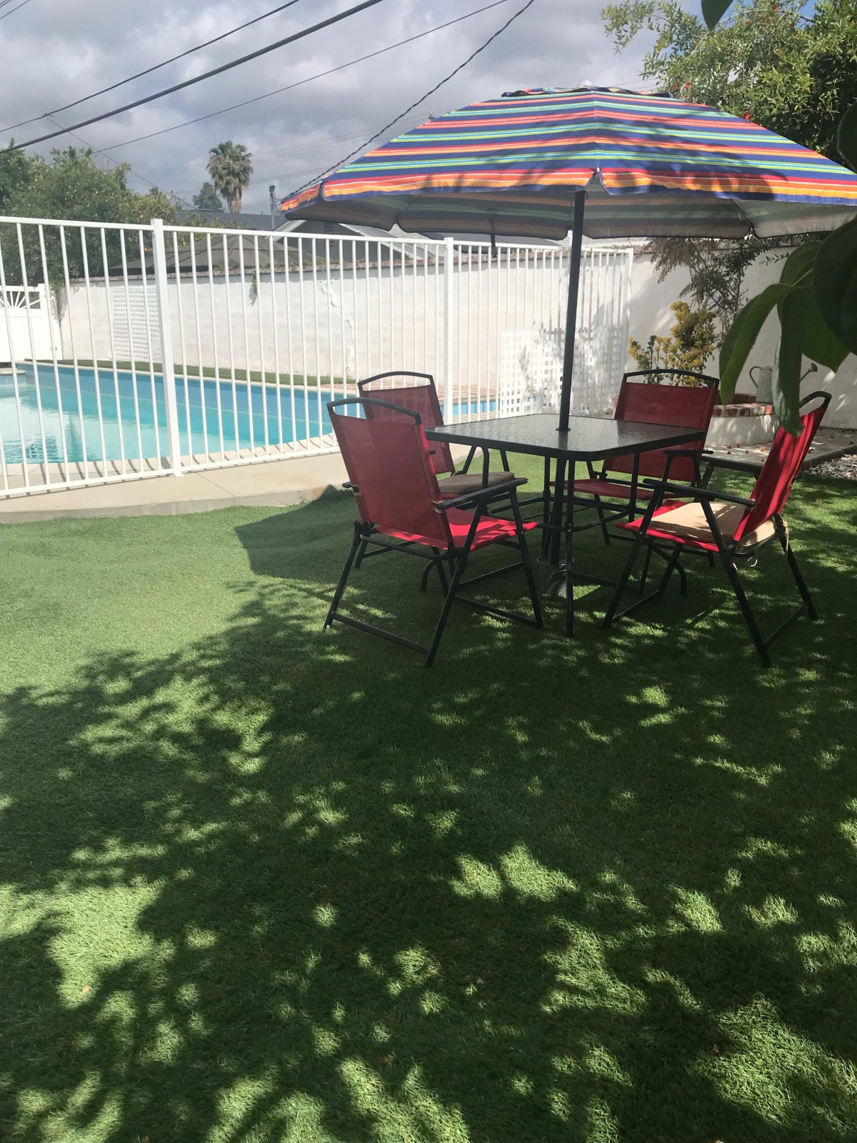 A sunny outdoor patio area with a table, chairs, and an umbrella near a swimming pool.