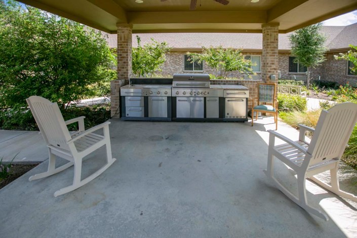A cozy outdoor patio with rocking chairs and a grill under a covered area.