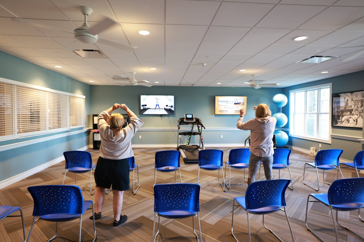 People participating in an indoor exercise class while following along with videos on screens.