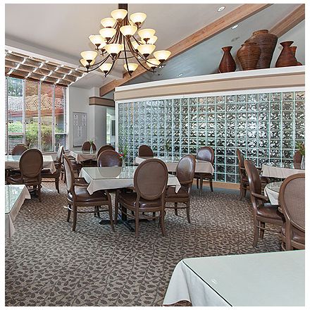 A well-appointed dining area featuring elegant tables and chairs beneath a stylish chandelier, with a decorative glass wall in the background.