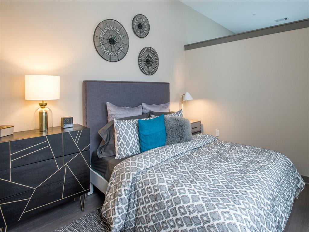 A modern bedroom featuring a stylish bed with patterned bedding, decorative pillows, and wall art.