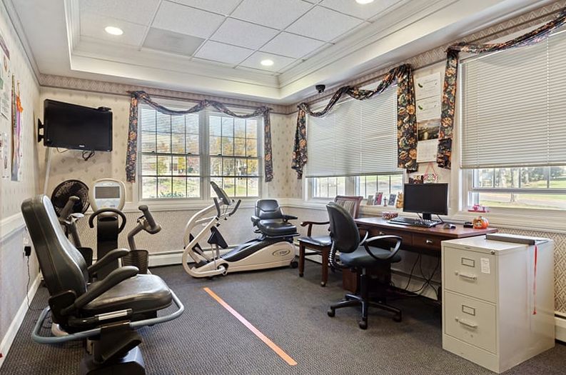A well-lit office space featuring desks, computers, chairs, and exercise equipment.