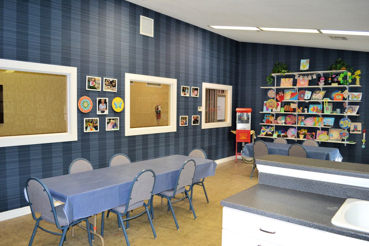 A cozy children's playroom with tables, chairs, a bookshelf, and a popcorn machine.