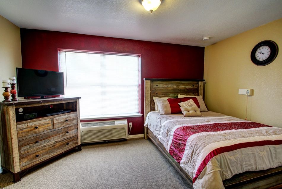 A cozy bedroom with a red accent wall, featuring a bed, dresser, and TV.