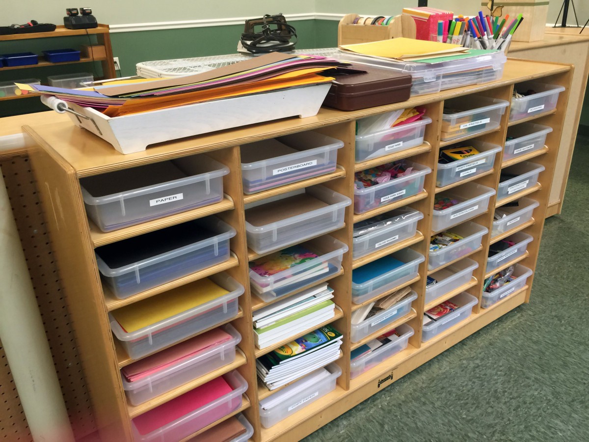 A neatly organized shelving unit containing various classroom supplies and paper.