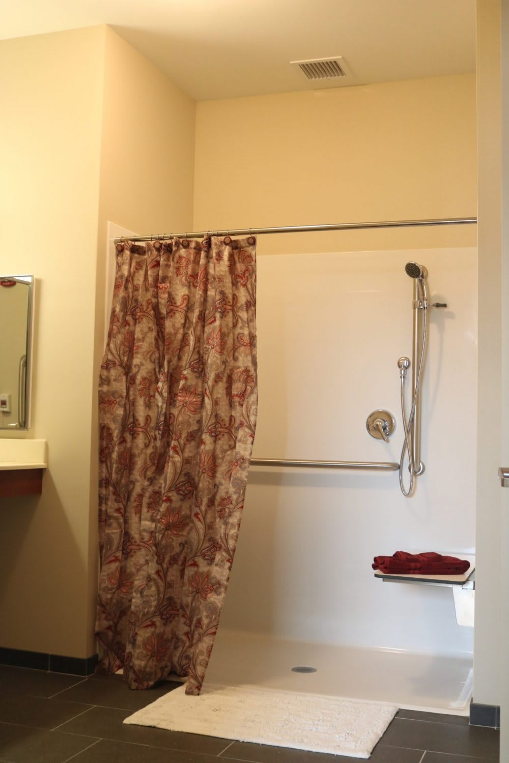 A bathroom featuring a shower with a floral curtain and safety grab bar.