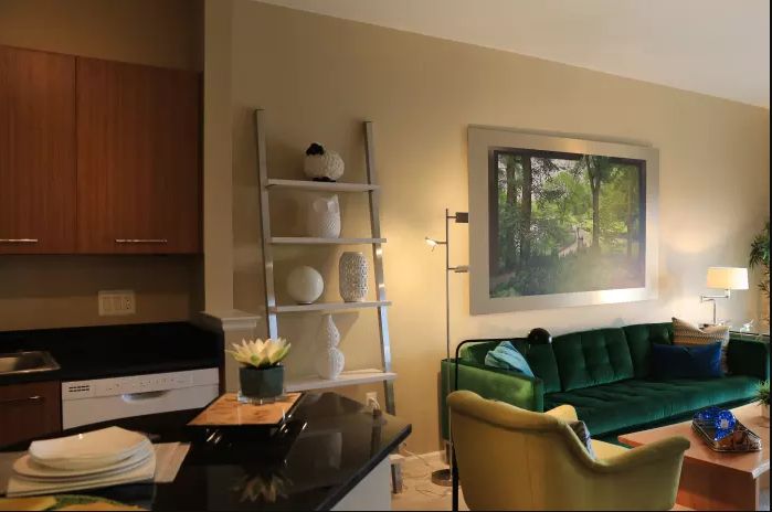 A modern living room featuring a green sofa, ladder-style shelf, and contemporary artwork.