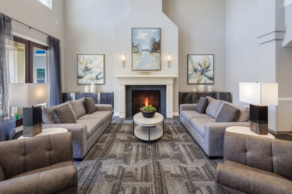 A modern living room with a central fireplace, surrounded by two gray sofas and decorative art on the walls.