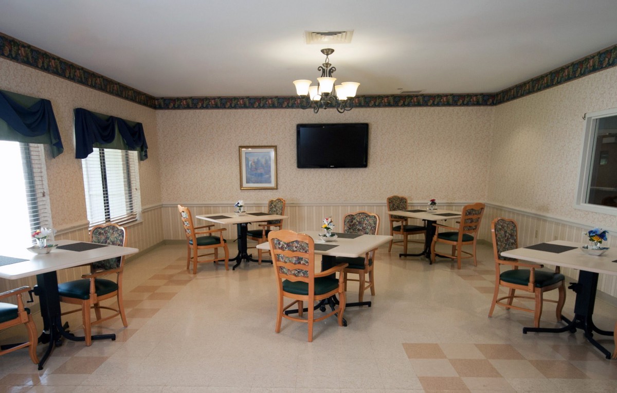 A well-lit dining area with several tables and chairs, featuring a television on the wall.