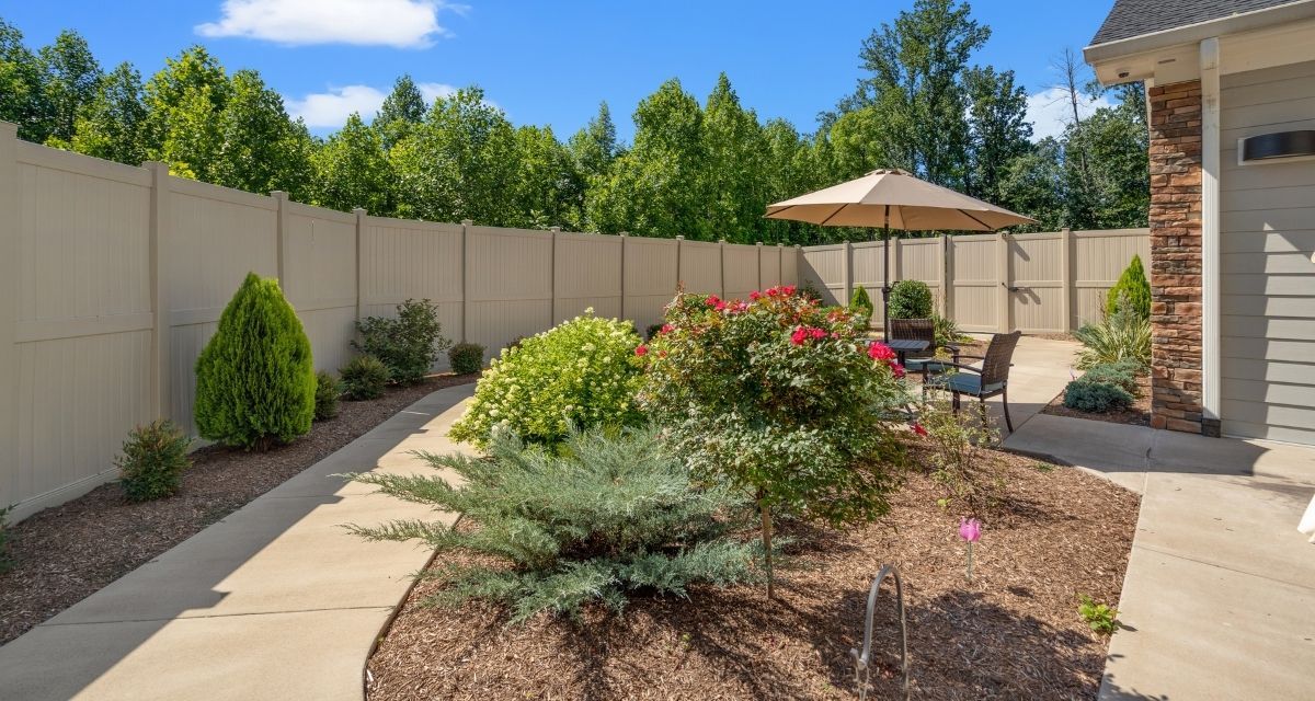 A beautifully landscaped backyard garden with a paved pathway, vibrant flowers, and outdoor seating under an umbrella.
