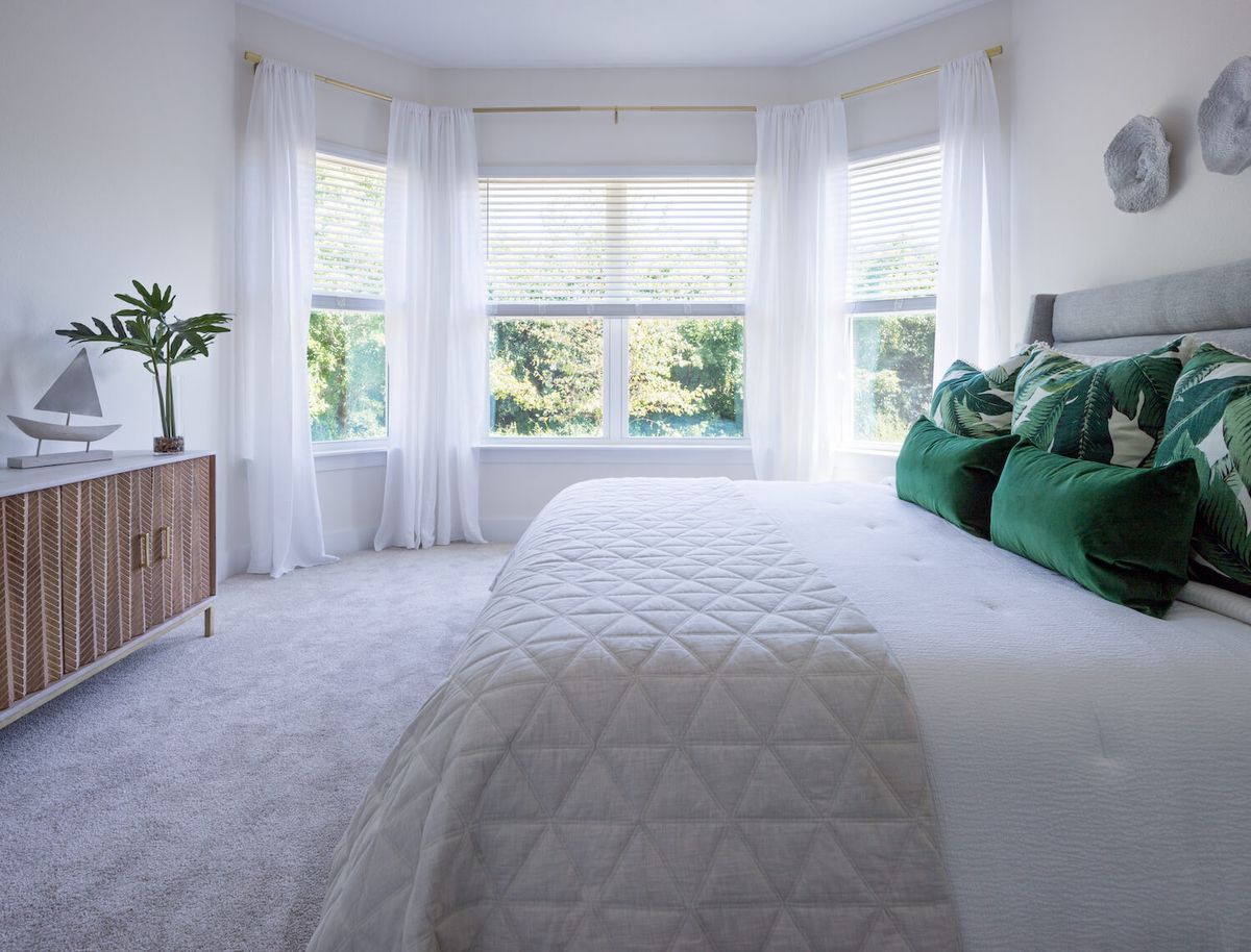 A modern and minimalist bedroom with a white and green color scheme, featuring large windows that allow for abundant natural light.