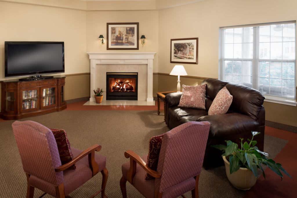 A cozy living room with a fireplace, featuring a sofa, armchairs, and a television.