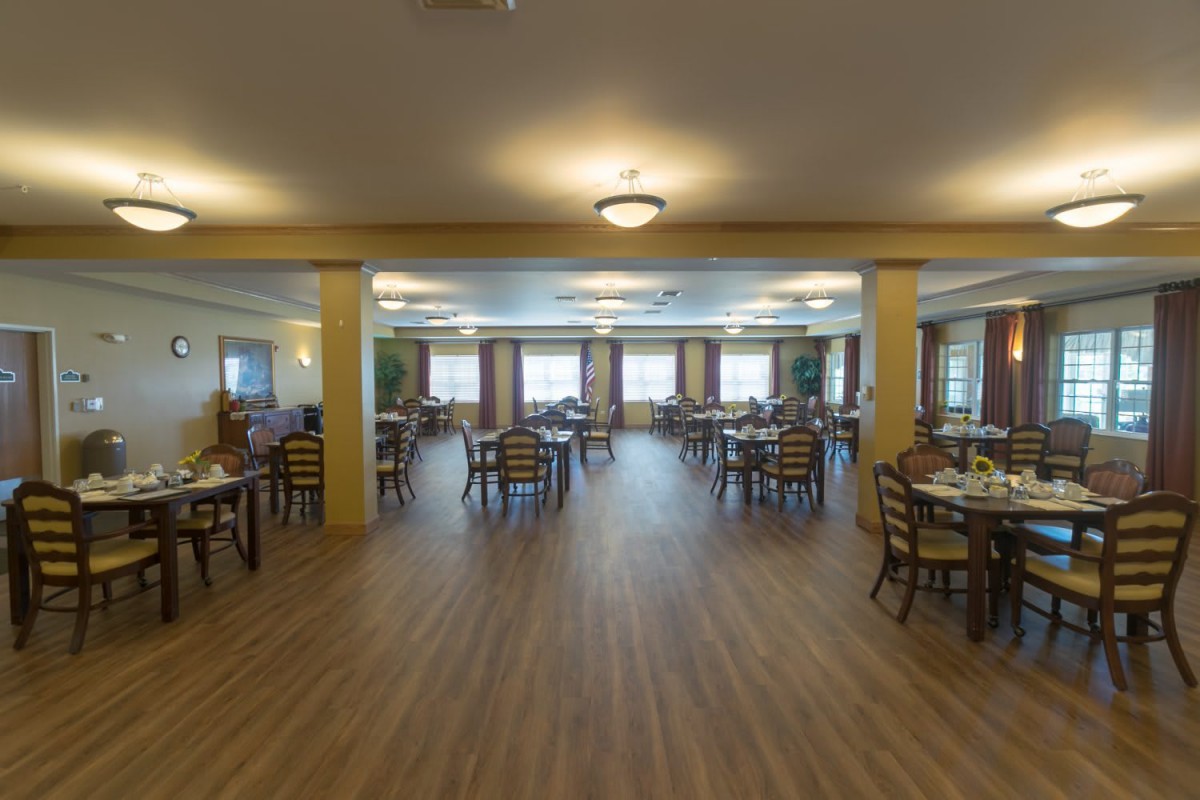 A spacious dining room with wooden floors, tables, and chairs arranged neatly under soft lighting.