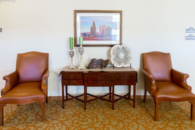 A cozy seating area featuring two leather chairs and a decorated table with a cityscape painting above.
