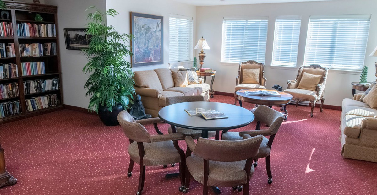 A cozy living room with a round table surrounded by chairs, a comfortable sofa, and a lamp.