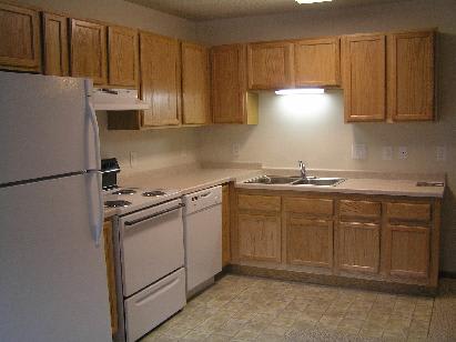 A simple kitchen with wooden cabinets, a refrigerator, stove, and sink.
