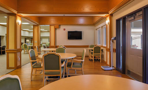 A spacious and well-lit dining area in a rehabilitation center, equipped with tables, chairs, and a television.