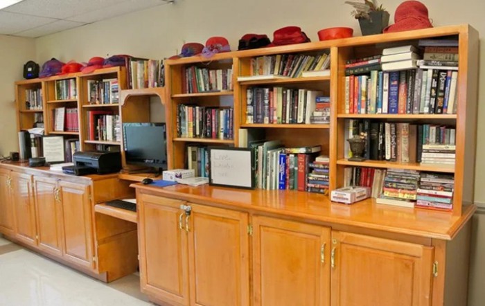 A wooden bookshelf filled with books and topped with a collection of hats, alongside a computer station.