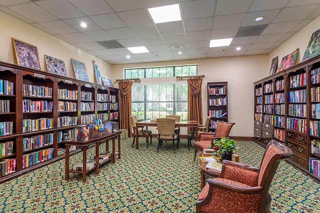 A cozy library room with bookshelves, comfortable chairs, and a large window.