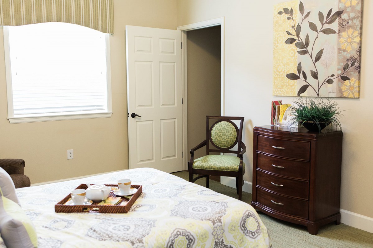 A cozy bedroom interior with a bed, chair, and dresser.