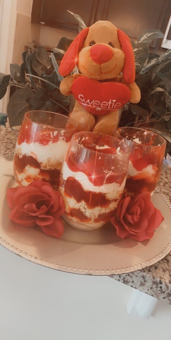 A delicious display of strawberry parfaits with creamy layers, accented by red roses and a cute teddy bear.